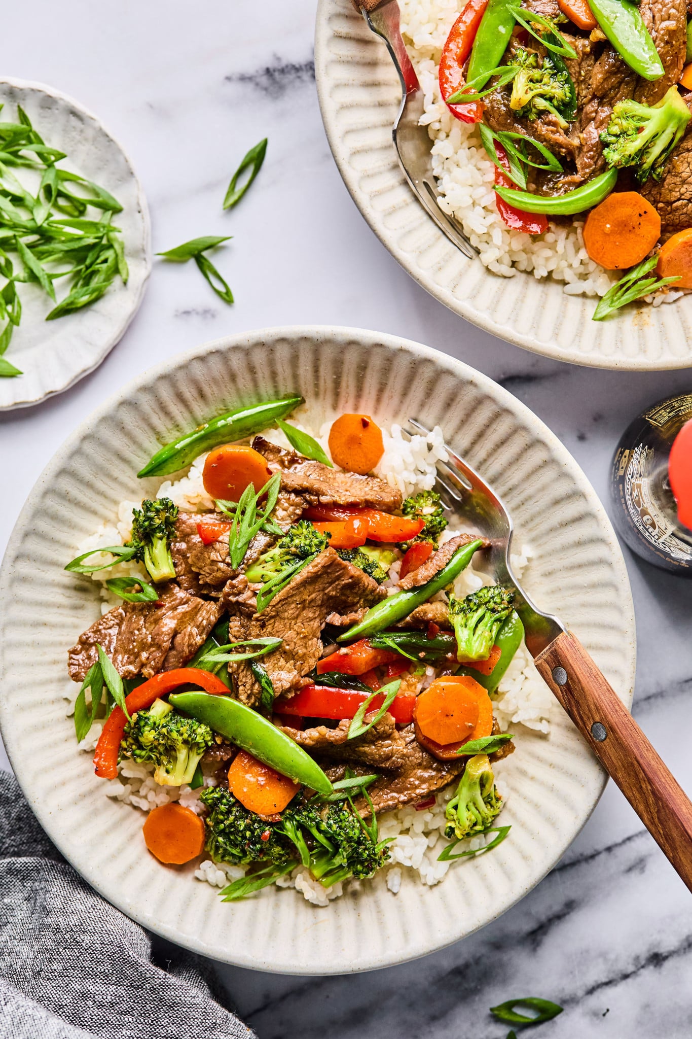 Top-down view of two ceramic bowls filled with beef and veggie stir fry served over white rice, garnished with fresh green onions.