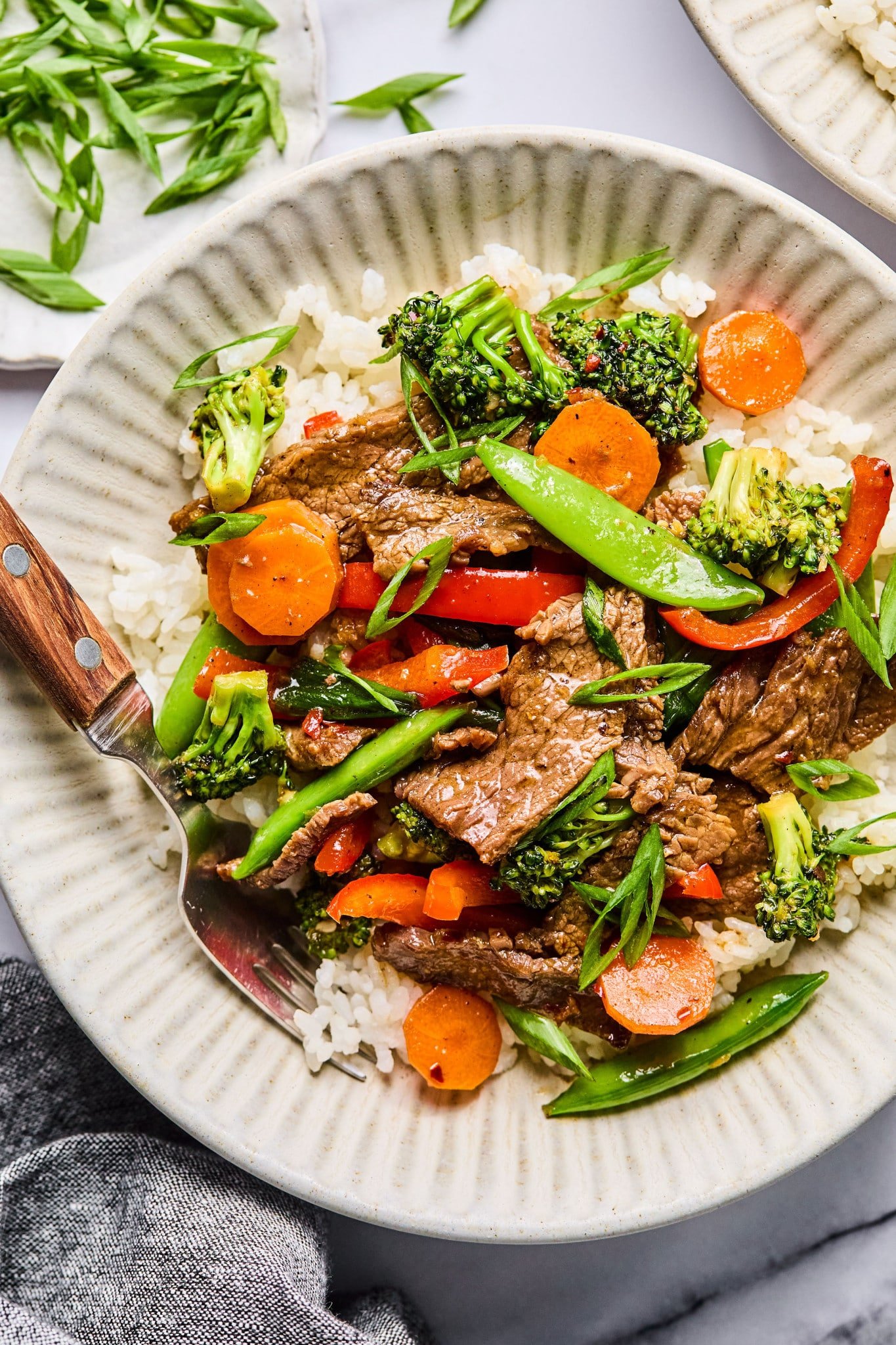 Close-up overhead of a single bowl filled with beef stir fry and rice, showing colorful veggies, beef, and a sprinkle of green onion slices.