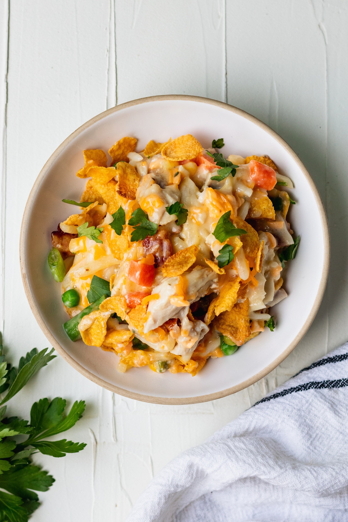 hash brown casserole in a white bowl garnished with fresh parsley and topped with corn flakes