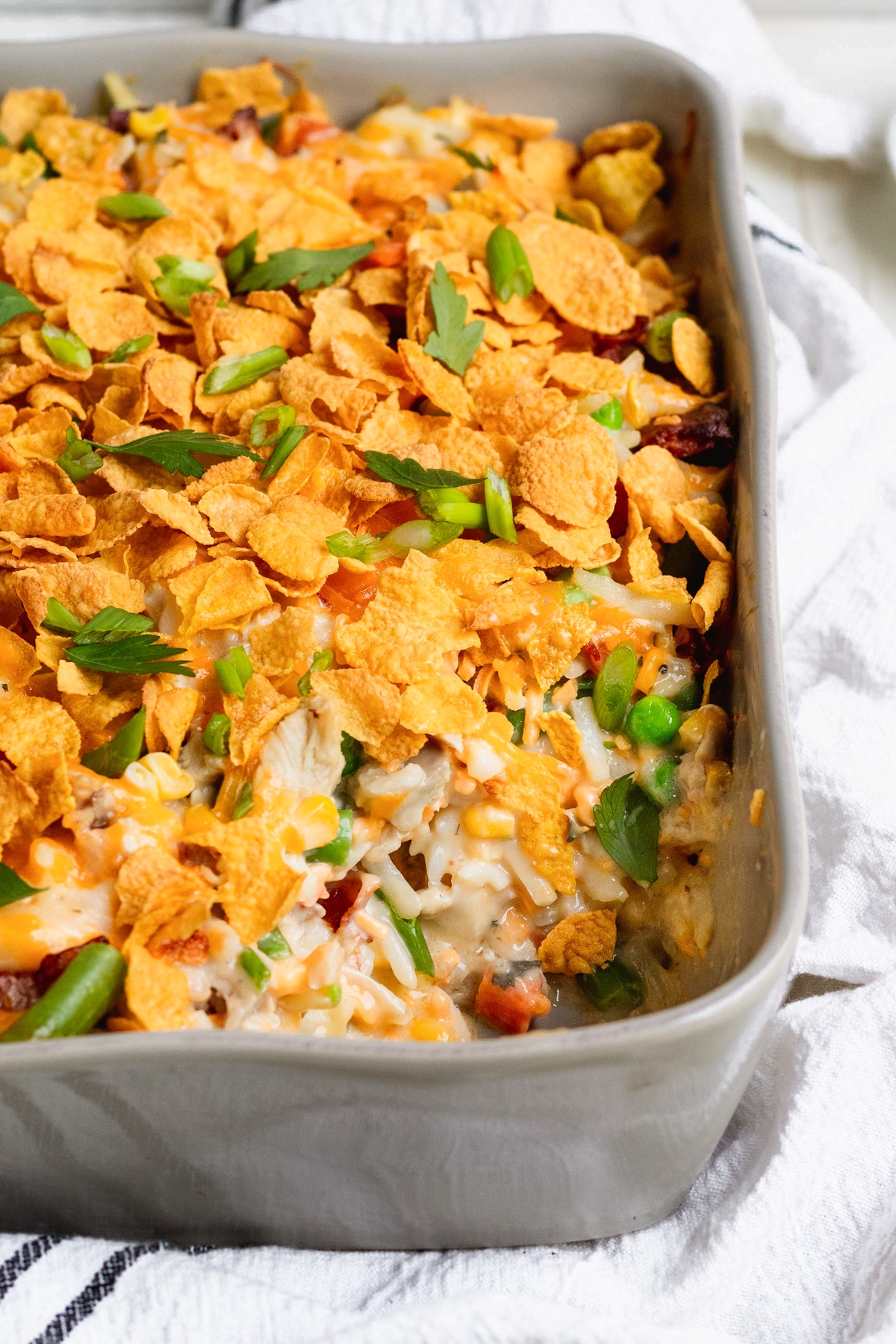 hash brown casserole in a grey casserole dish garnished with fresh parsley and topped with corn flakes