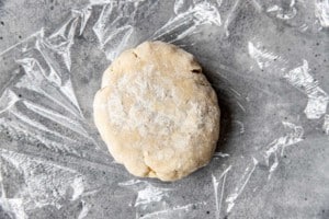 mound of pie dough with flour on clear plastic wrap on a gray counter