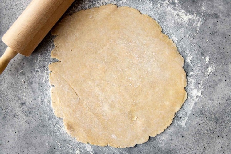 pie dough rolled flat on a gray countertop with flour sprinkled underneath