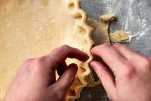 hands pinching pie dough in a pie pan