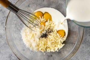 clear bowl with cheese, milk, eggs, and spices with a whisk