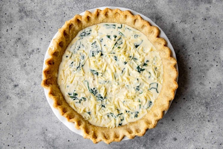a pie dish with uncooked spinach quiche