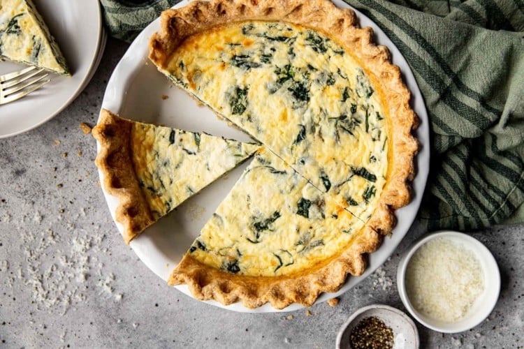a pie pan with spinach quiche with two slices missing