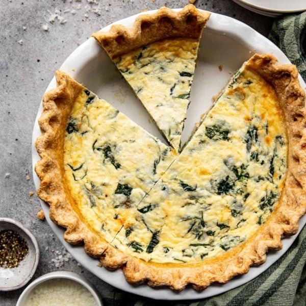 spinach quiche with two pieces missing in a white pie pan
