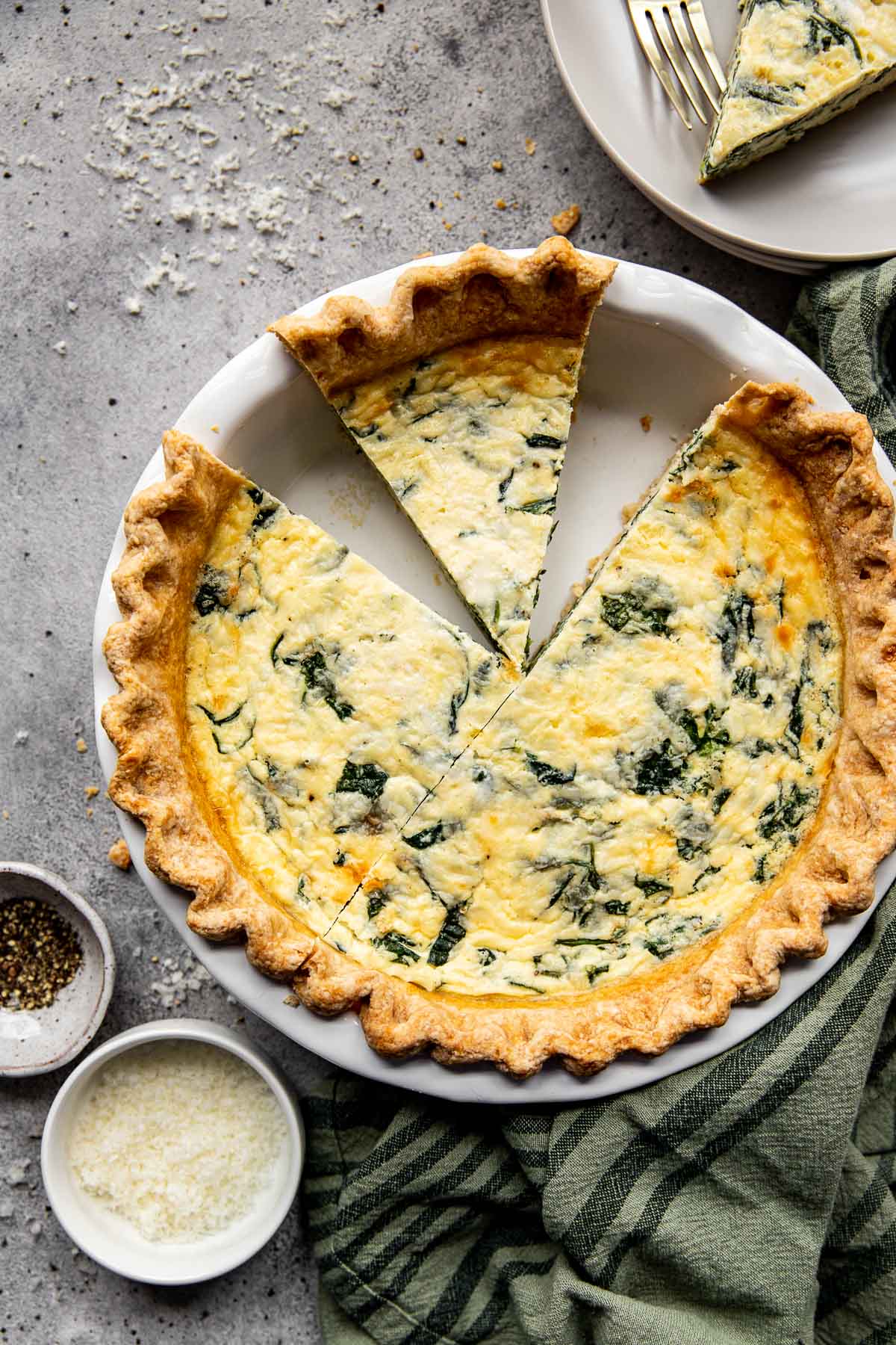 spinach quiche with two pieces missing in a white pie pan