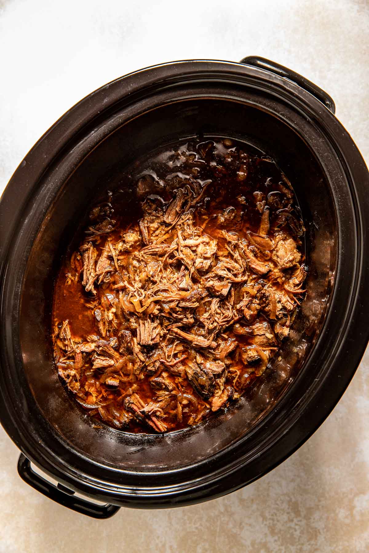 shredded beef in a black slow cooker. 