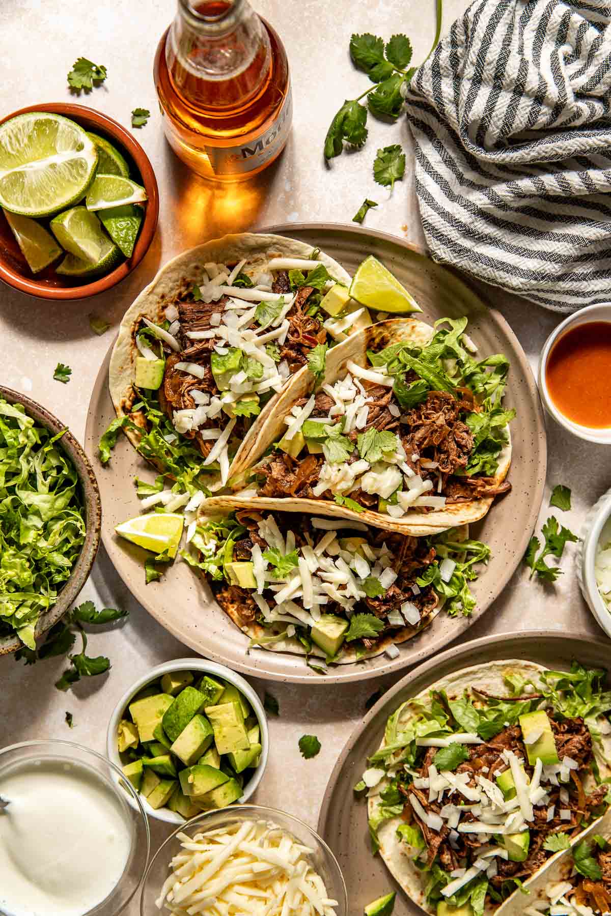 shredded beef tacos on a plate with fresh cilantro, cheese, and limes. 