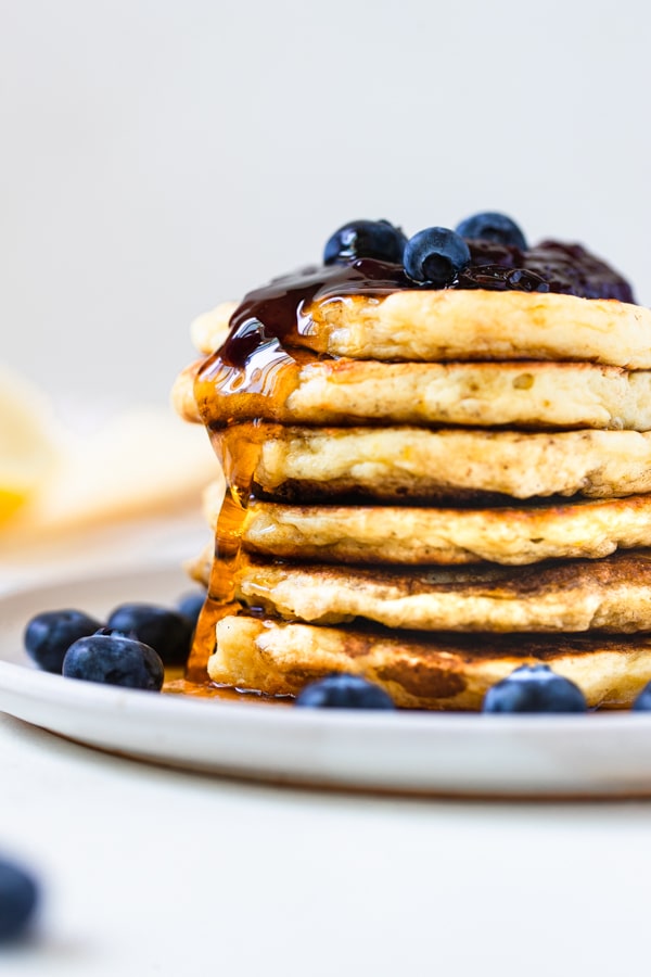 stacked lemon blueberry pancakes on a plate with maple syrup on top