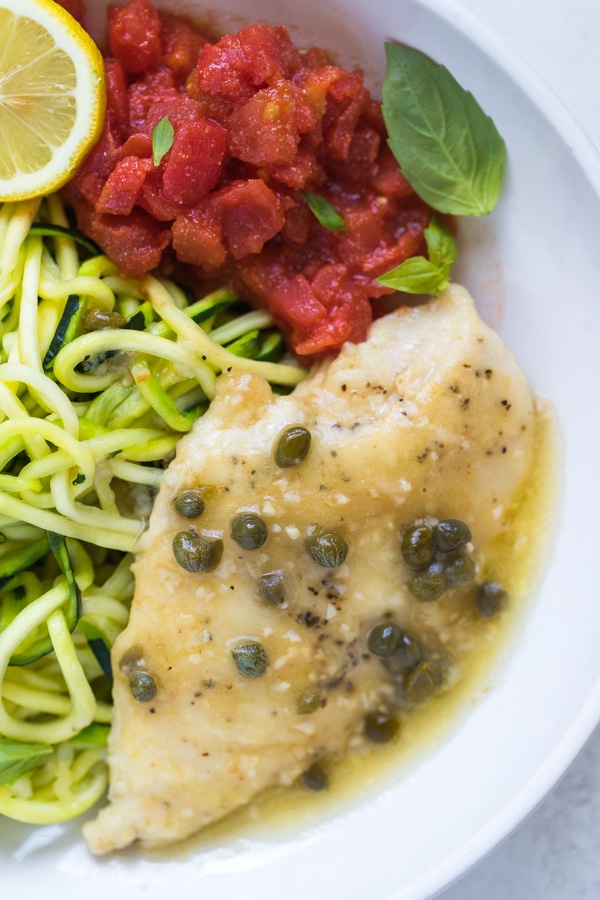 piccata topped with capers in a white bowl with zoodles