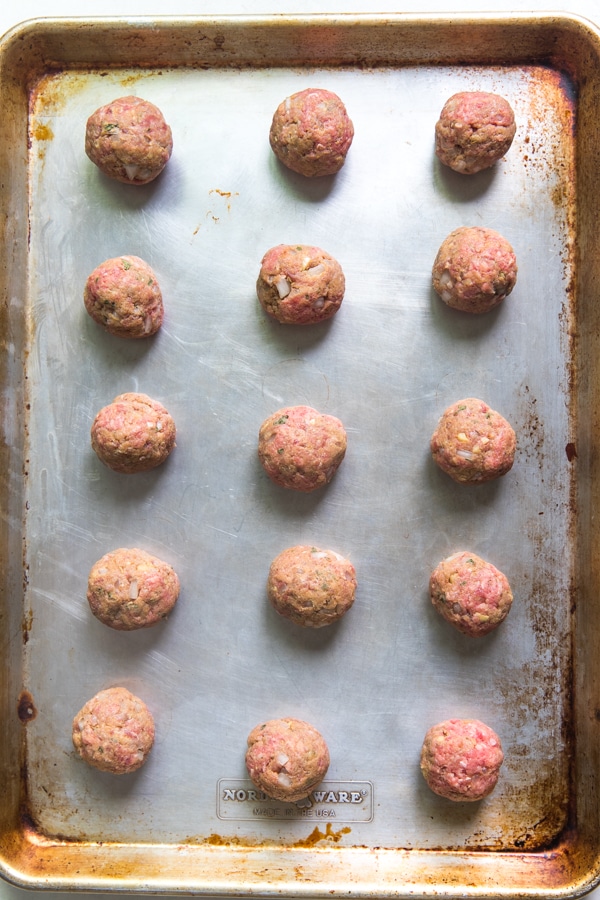 uncooked ground beef meatballs on a rimmed baking sheet