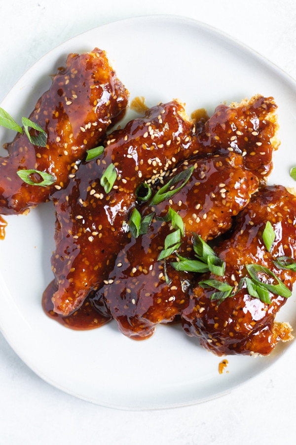 sesame chicken on a white plate with sesame seeds and green onions on top