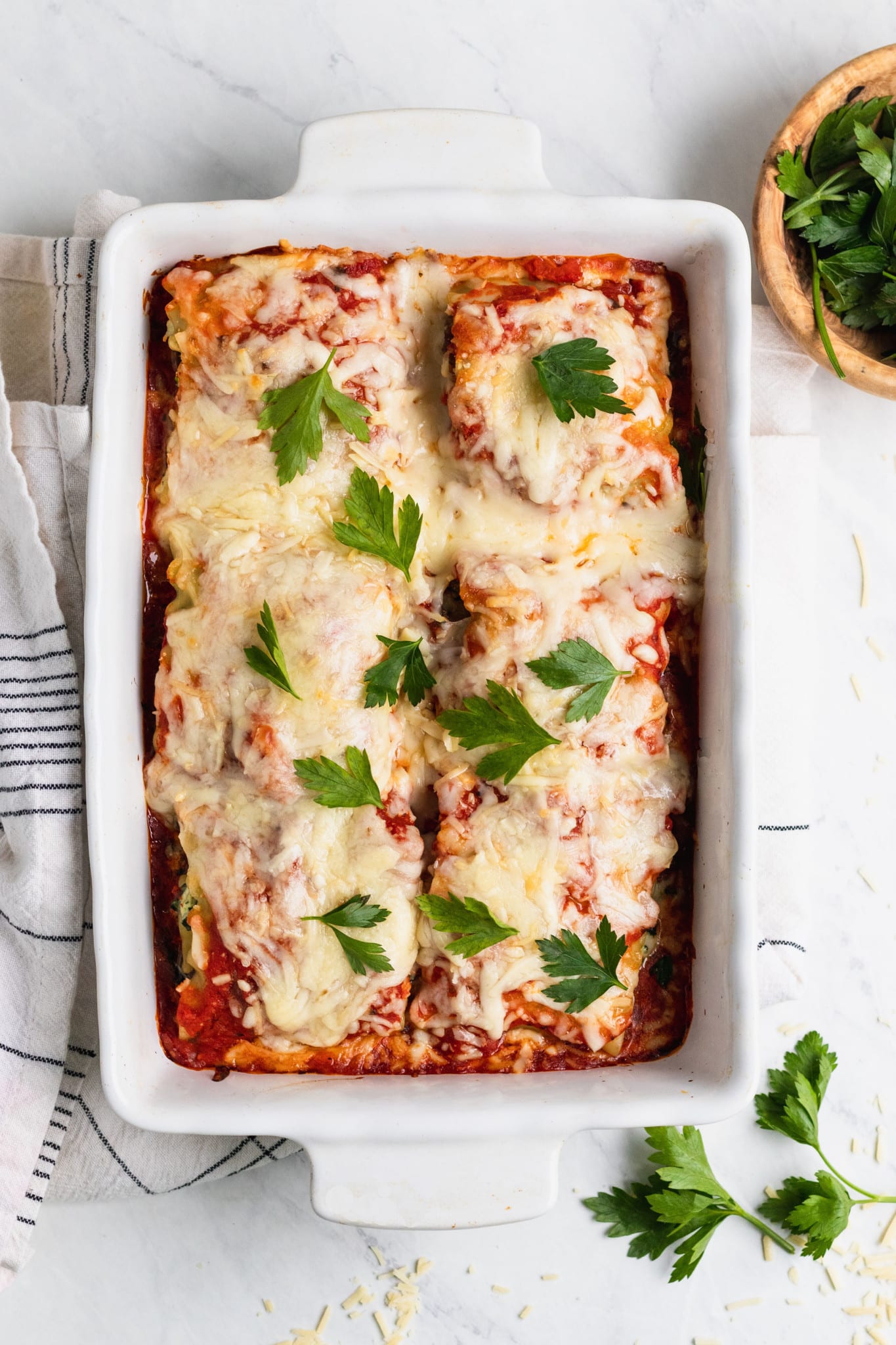 cheesy spinach ricotta rolled up into a lasagna noodle covered in red sauce in a casserole dish