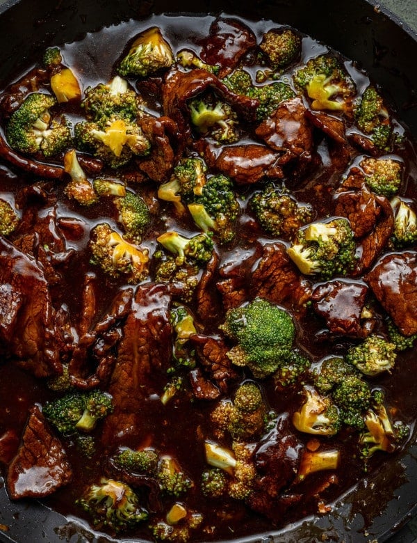Close-up of beef and broccoli stir-fry in a dark sauce inside a skillet, showing tender beef slices and bright green broccoli coated in glossy sauce.