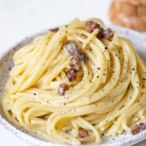 spaghetti carbonara on a speckled plate garnished with black pepper