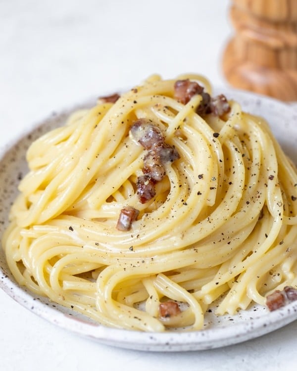 spaghetti carbonara on a speckled plate garnished with black pepper