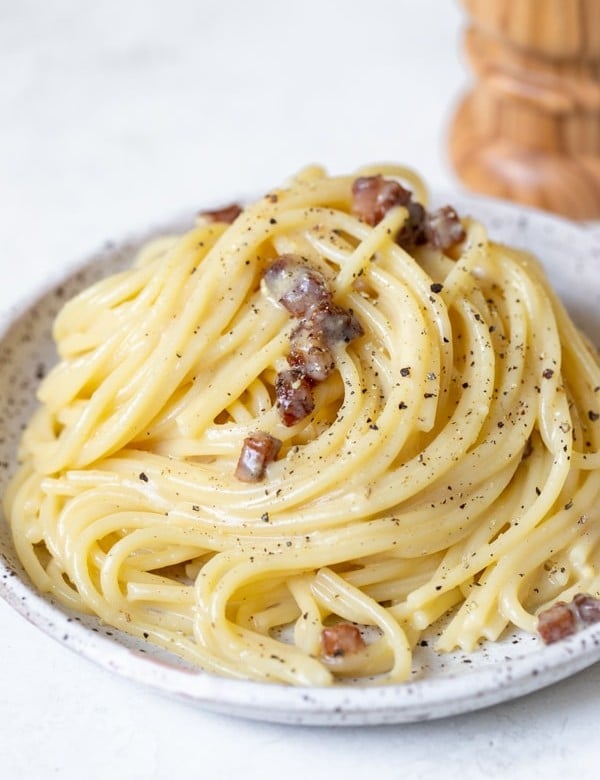 spaghetti carbonara on a speckled plate garnished with black pepper