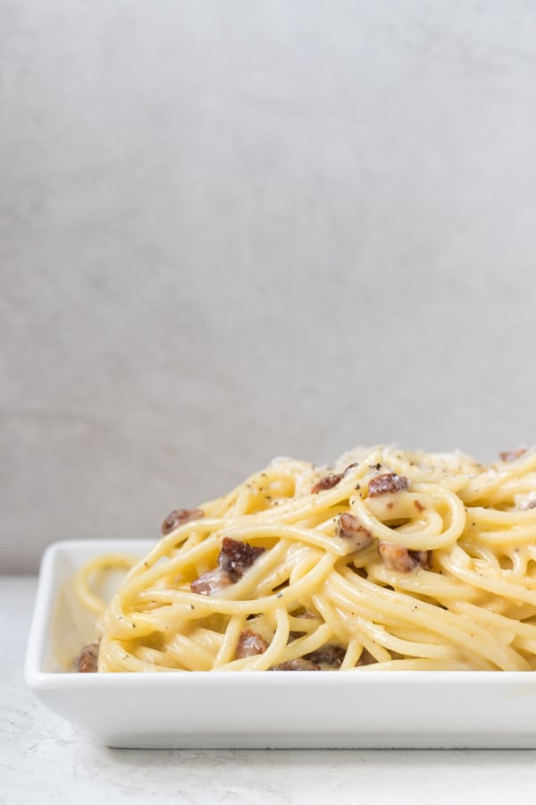 spaghetti carbonara on a white plate garnished with black pepper