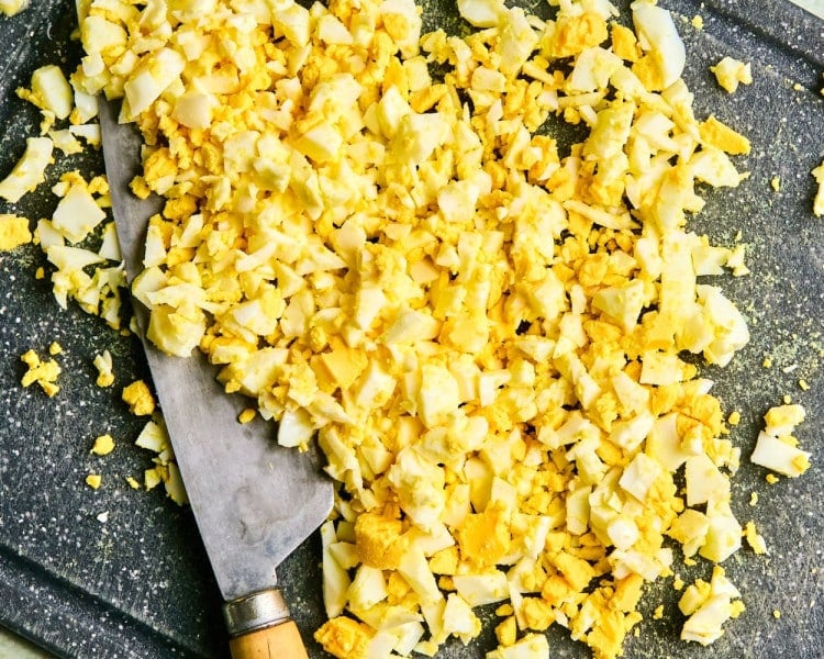 Chopped hard boiled eggs on a black cutting board.