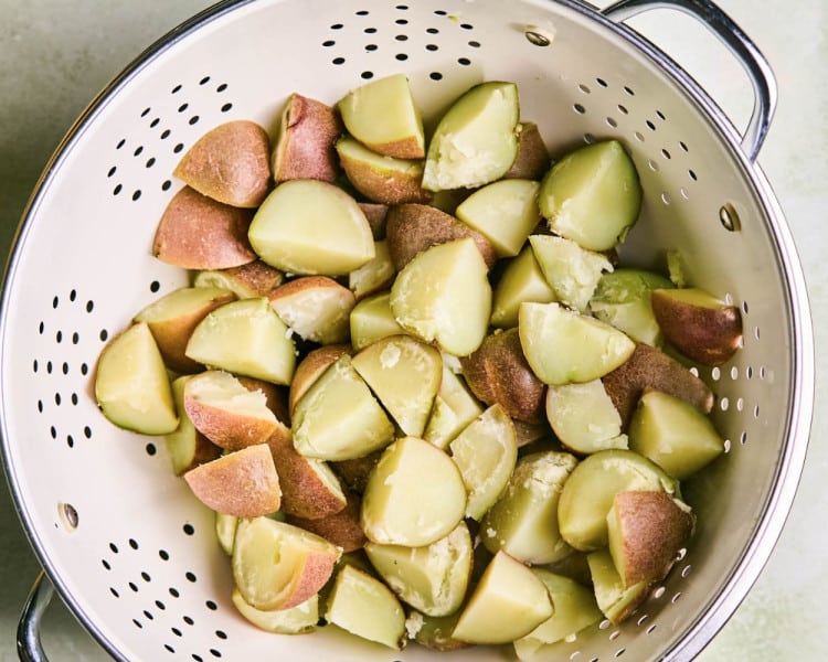 Boiled, chopped red potatoes in a white colander.