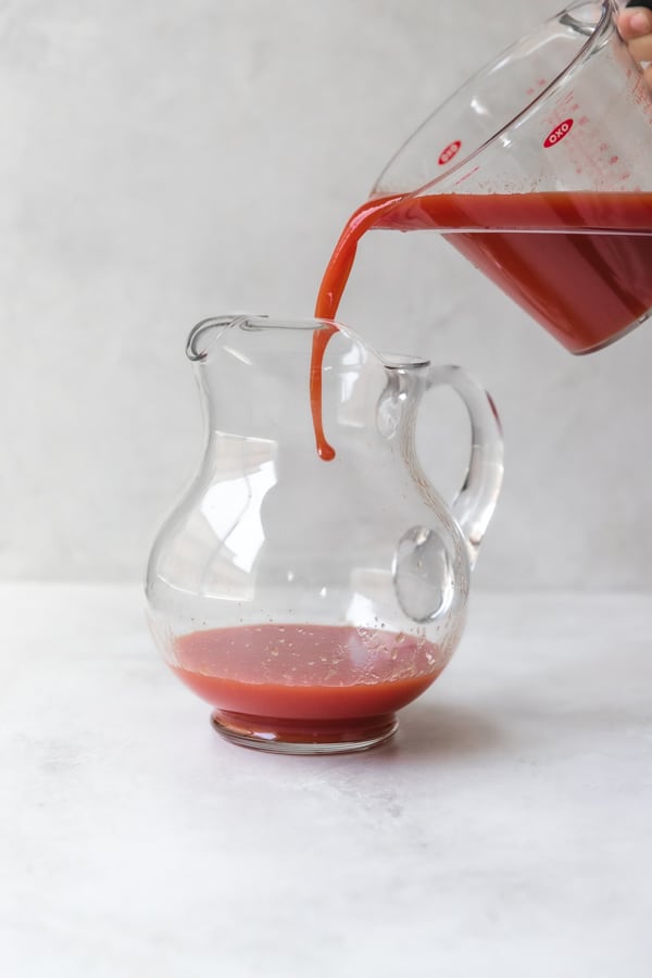 tomato juice being poured into a glass pitcher 