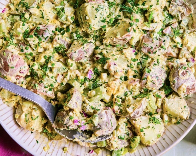 Bowl of red potato salad with dressing and chopped herbs.