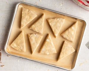 Unbaked maple scone wedges arranged on a parchment-lined baking sheet, ready to be baked.
