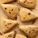 Overhead shot of freshly baked maple scones with smooth maple glaze and pecan pieces on parchment paper, showing their flaky texture.