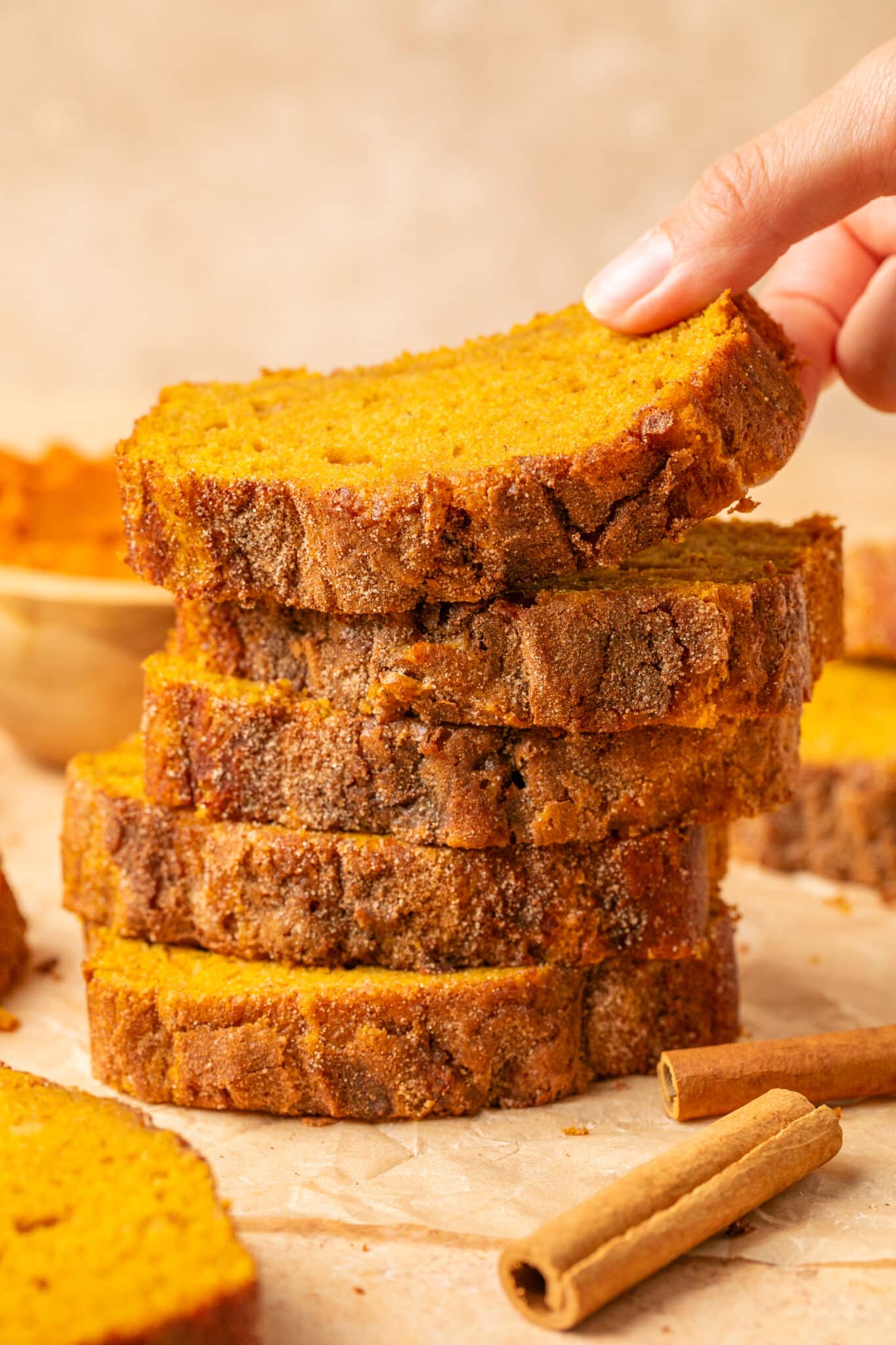 a womans hand picking up a slice of pumpkin bread. 