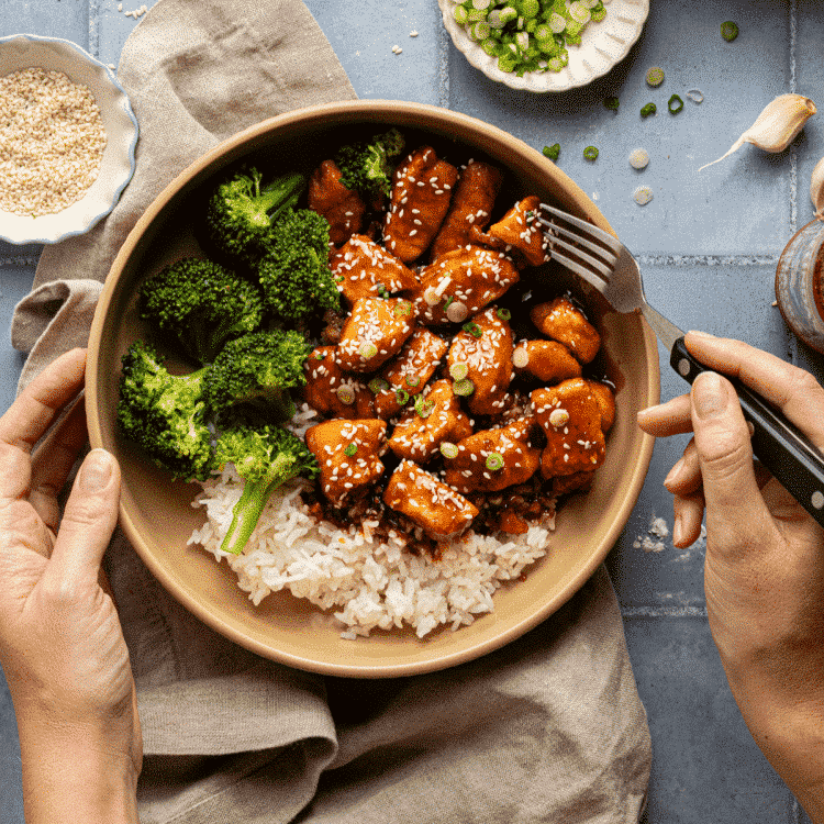 Honey garlic chicken in bowl with rice and broccoli with fork digging in.