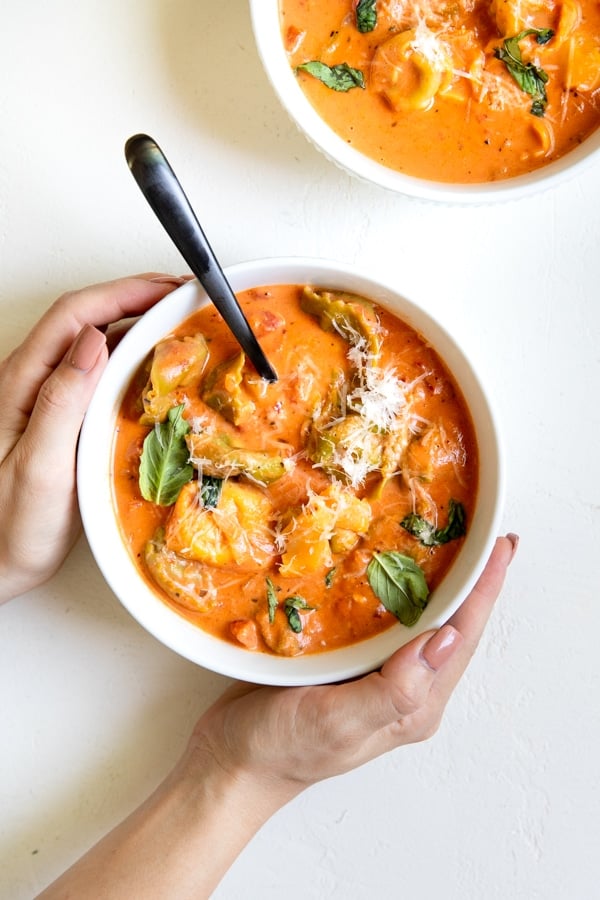 tomato soup with tortellini in a white bowl topped with parmesan cheese and basil