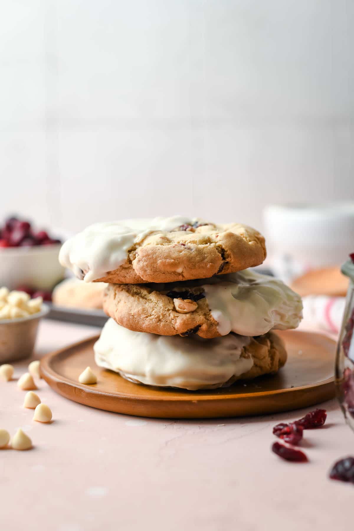 a stack of white chocolate cookies on a brown plate with cranberries