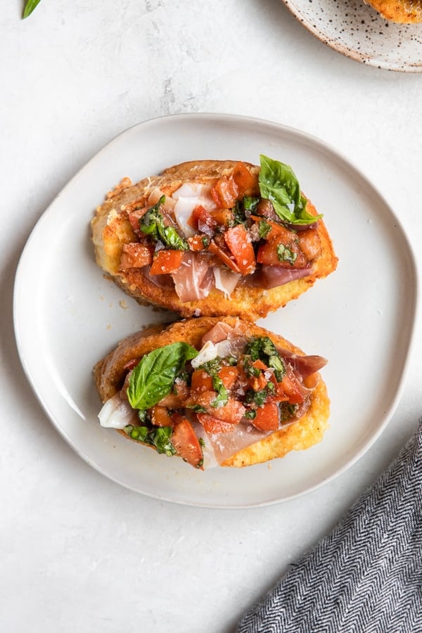 a slice of french toast with Prosciutto, tomatoes and basil on a white plate