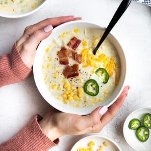 a bowl of Jalapeño Corn Chowder topped with bacon and cheese and a hands holding the bowl