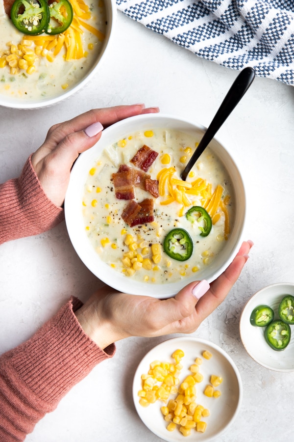 a bowl of Jalapeño Corn Chowder topped with bacon and cheese and a hands holding the bowl