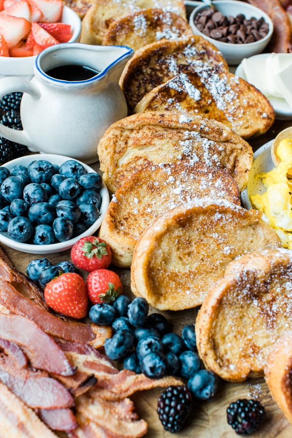 french toast on a cutting board with fresh berries, bacon and syrup