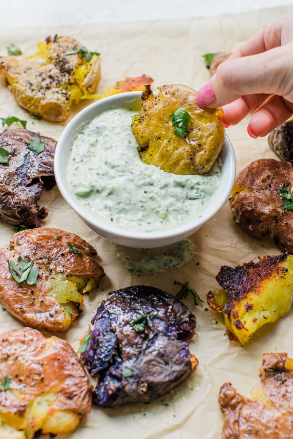 a girls hand dunking a smashed potato into aioli sauce