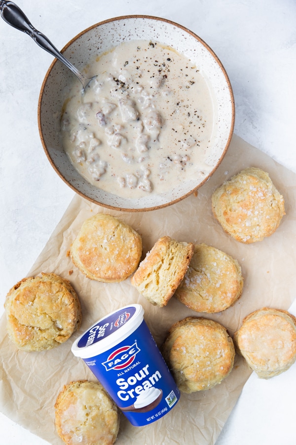 freshly baked biscuits on parchment paper next to a bowl filled with sausage gravy 
