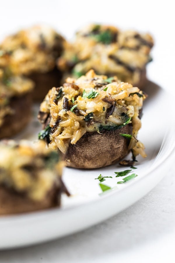 a wild rice stuffed mushroom on a white plate topped with parsley  