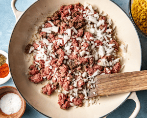 Adding uncooked ground beef and onions to large skillet.