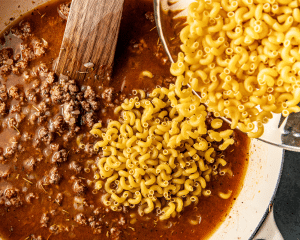 Adding the dry noodles to the beef broth and ground beef mixture.
