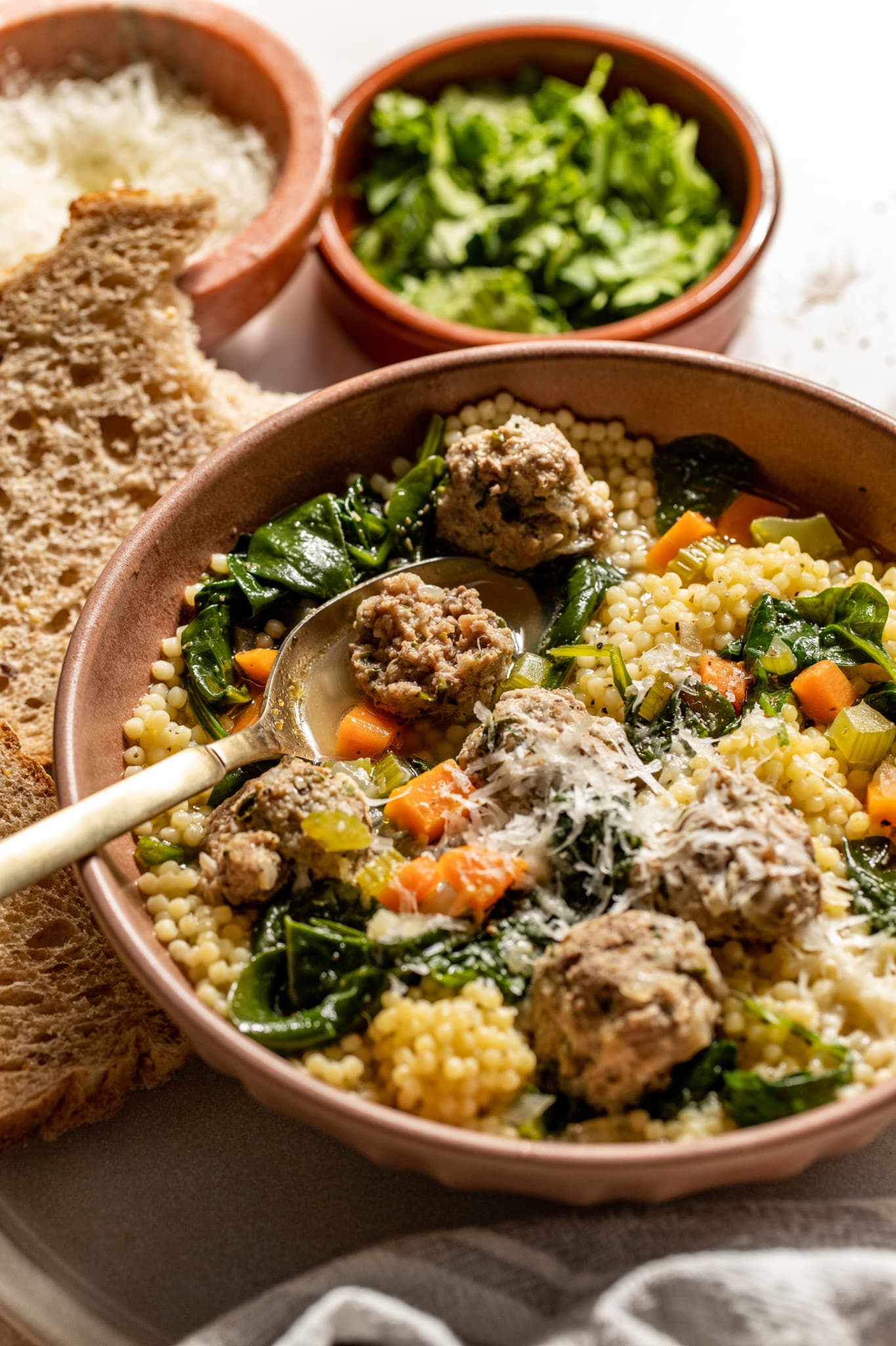 italian wedding soup in a bowl with fresh parmesan on top and a spoon taking a bite out of a meatball. 