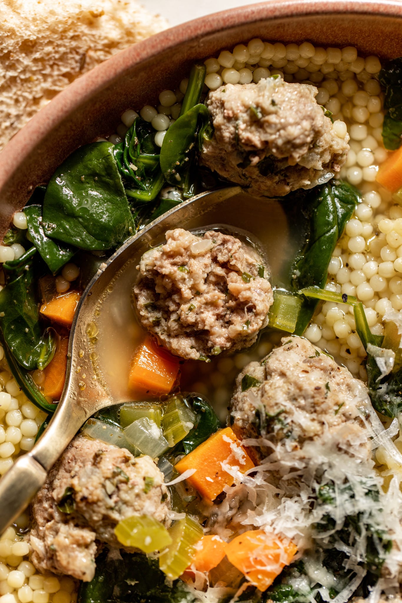 a close up image of italian wedding soup with a meatball on a gold spoon. 