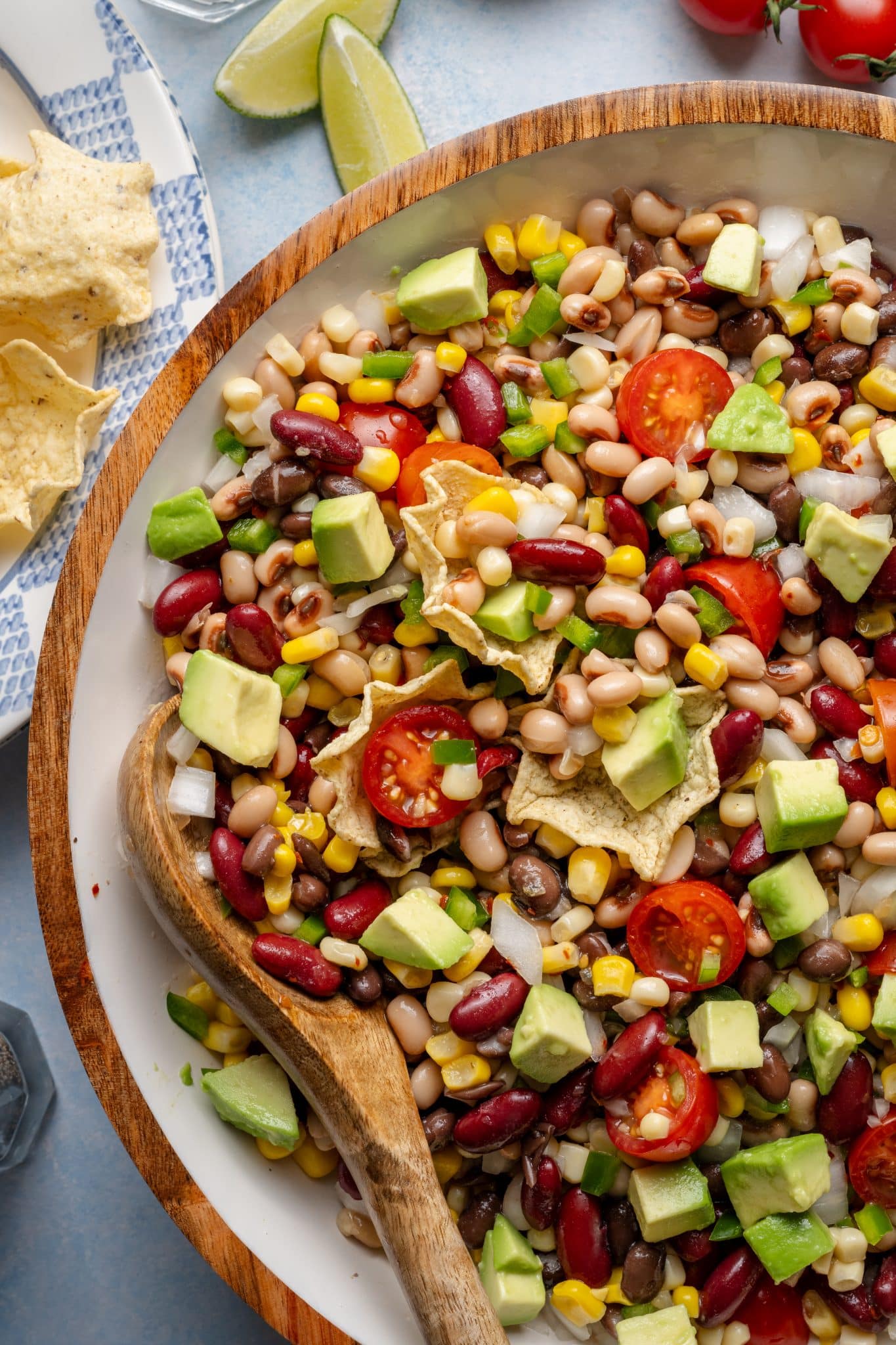Close-up of cowboy caviar in a wooden bowl with tortilla chips and a wooden spoon, showcasing fresh veggies, beans, corn, and avocado.