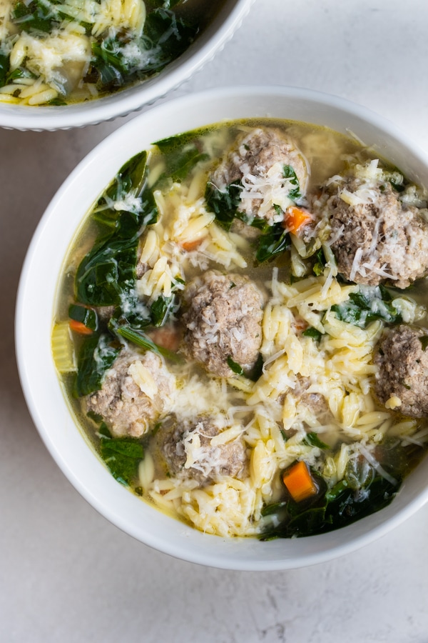 Italian wedding soup in a white bowl topped with cheese