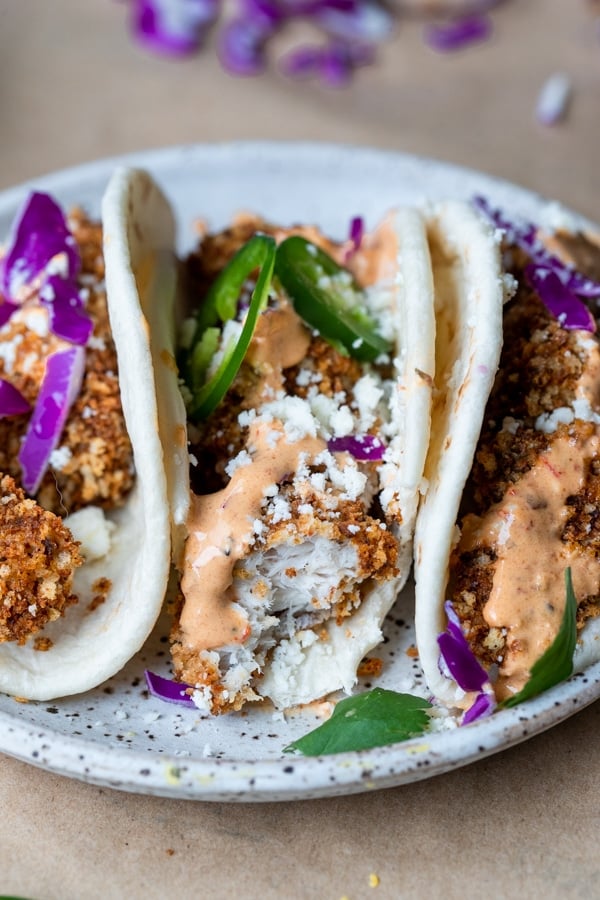 three flour tacos with breaded white fish, a light orange sauce, purple cabbage, and jalapenos