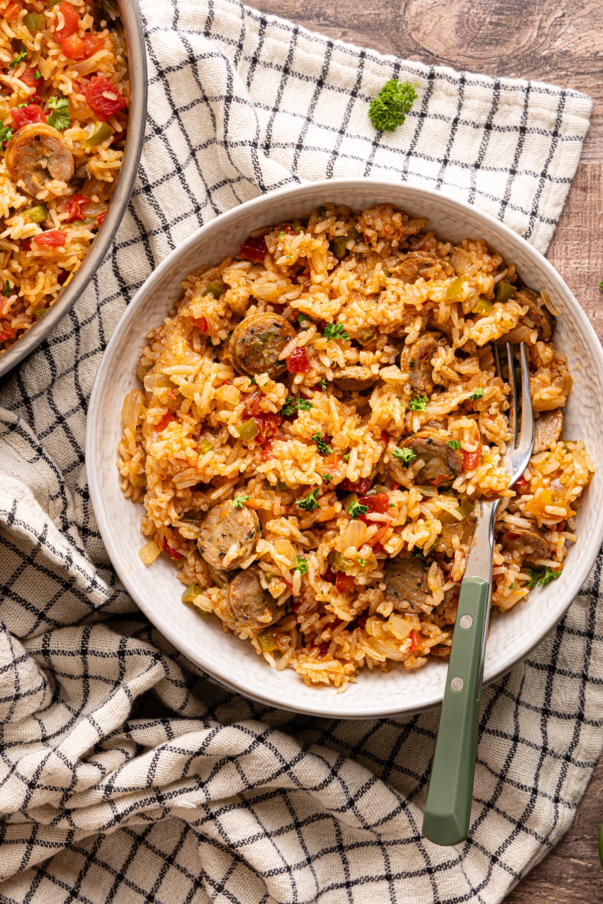 Serving bowl filled with sausage, peppers, and rice, garnished with parsley and placed on a neutral kitchen towel.