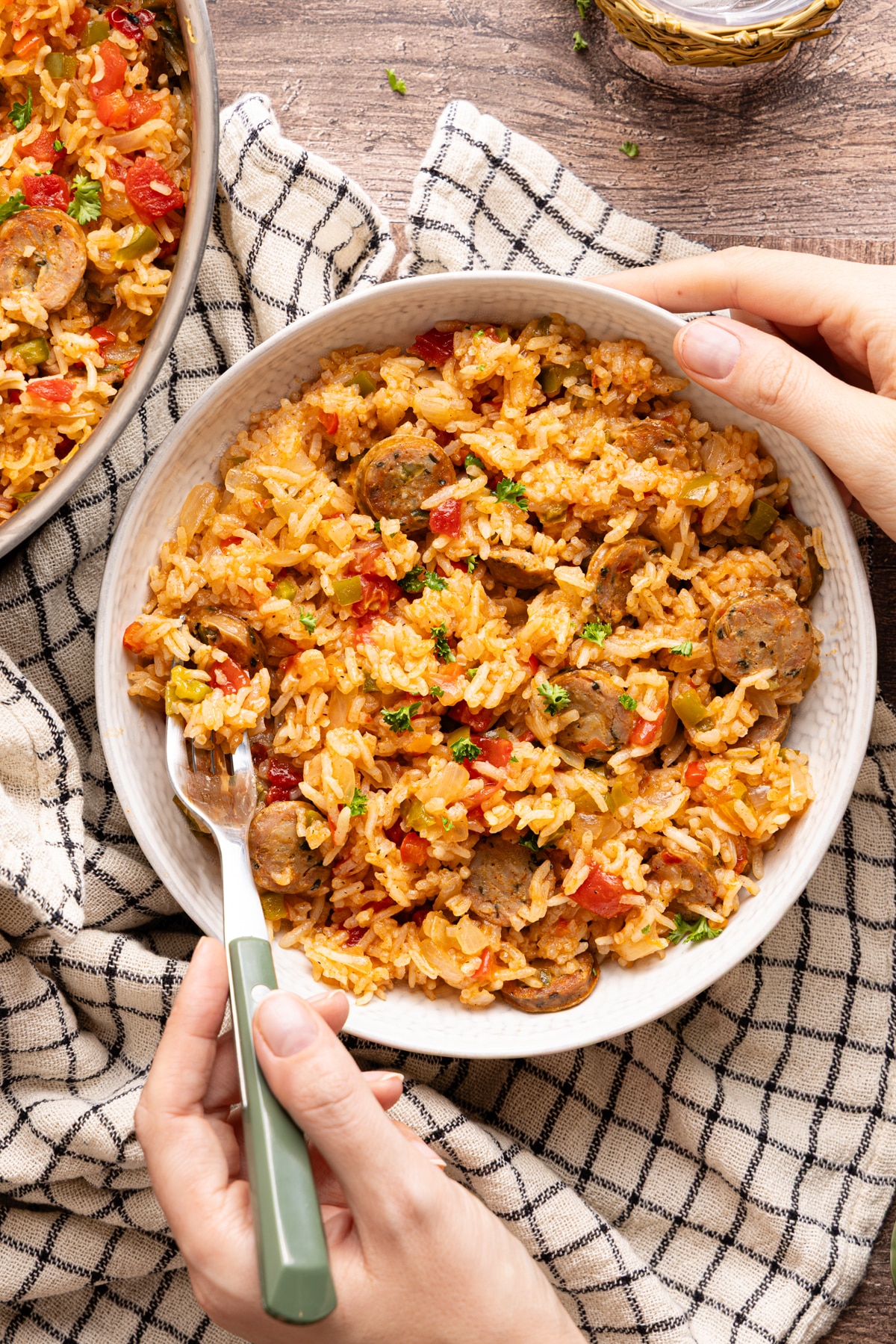 Hands holding a bowl of sausage, peppers, and rice with a fork, showing a close-up of the finished skillet meal ready to eat.